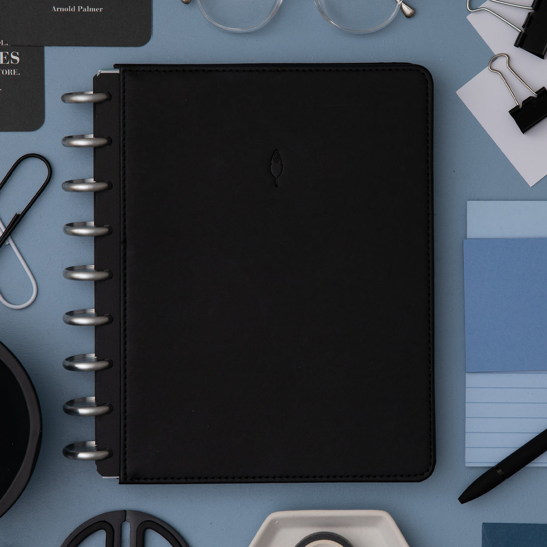 black faux leather cover with silver disc on this inkwell planner surrounded by office supplies
