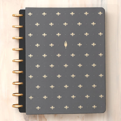 A hard cover featuring black background and busy bee design for this inkwell press 7x9 planner system featuring gold discs.