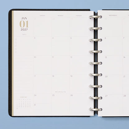 An open disc-bound planner showing a monthly calendar spread with lined notes section and reference calendar, and bullet points