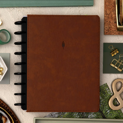 brown faux leather cover with black disc on this inkwell planner surrounded by office supplies