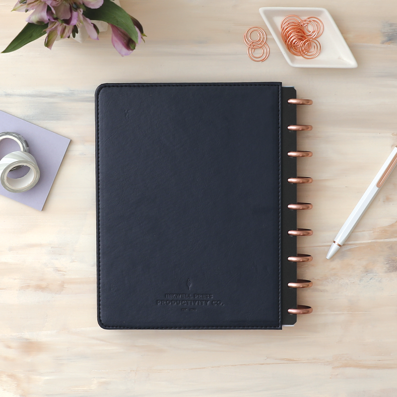Vegan leather deep navy blue cover with embossed quill logo, gold discs, and in a 7x9 planner size